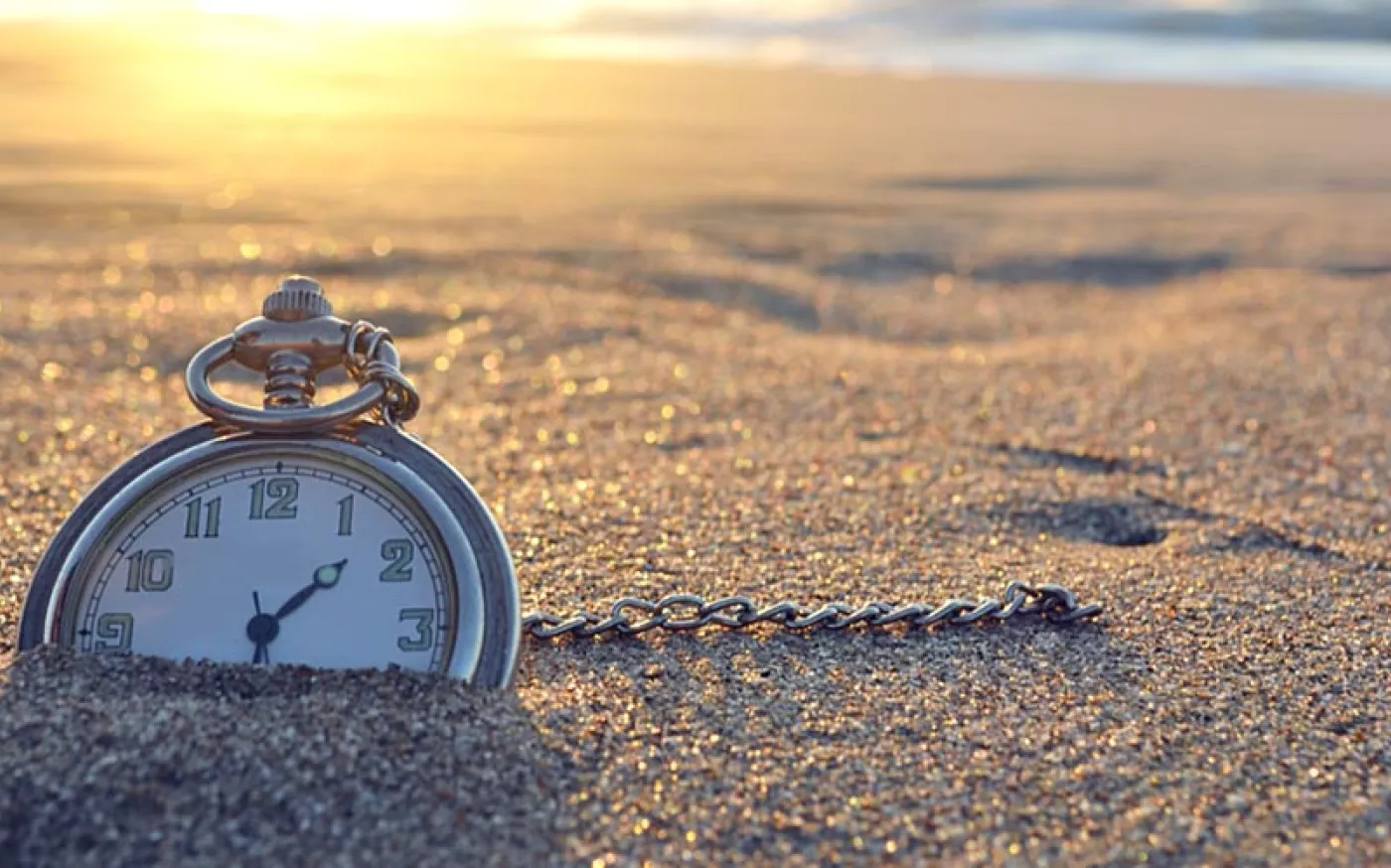 Pocket watch nestled in the sand of a beach at sunset